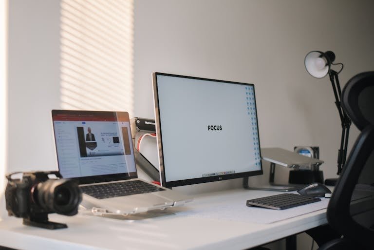 A clean and modern home office setup featuring a laptop, monitor, and camera on a white desk.