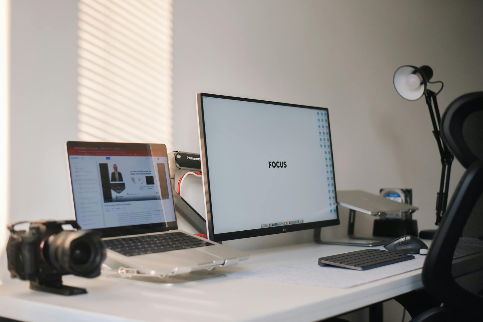 A clean and modern home office setup featuring a laptop, monitor, and camera on a white desk.