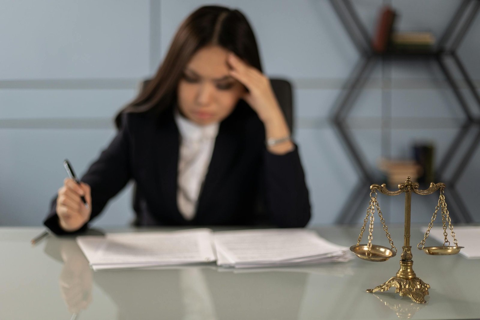A fatigued female lawyer reviewing documents with a justice scale nearby, emphasizing stress in legal work.