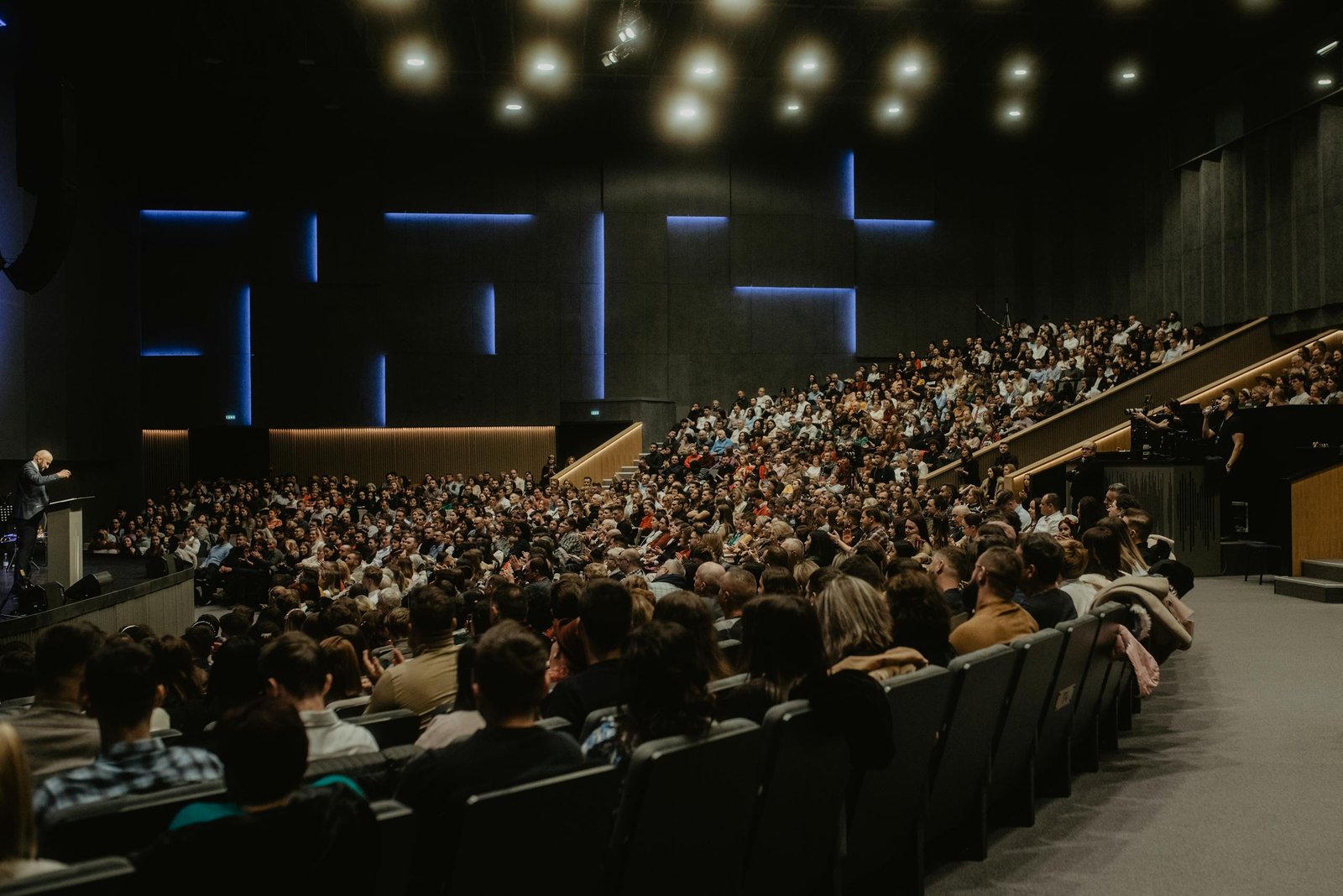 A large audience attentively listens to a speaker at a conference in Oradea, Romania.