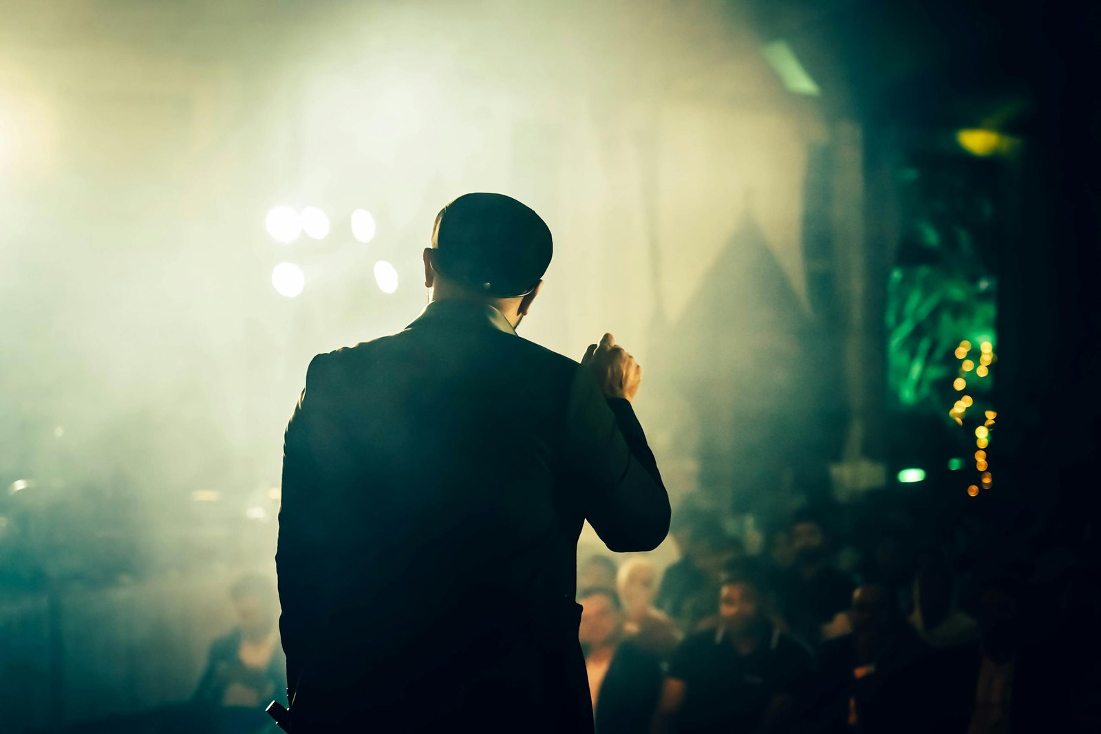 A man seen from the back speaking to an audience at an atmospheric entertainment venue.