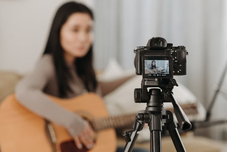 A woman plays guitar while recording a video indoors. Ideal for vlogs or music-related content.