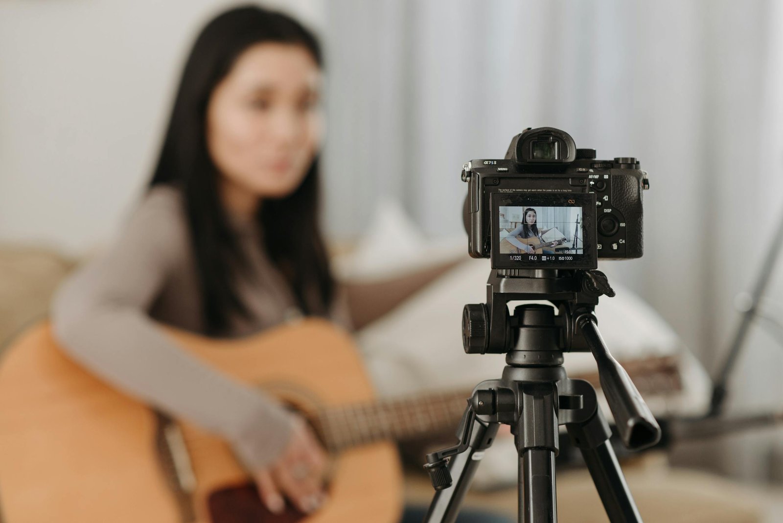 A woman plays guitar while recording a video indoors. Ideal for vlogs or music-related content.