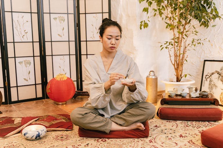 Asian woman meditating with a candle in a tranquil indoor setting, promoting relaxation and zen.
