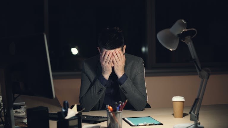 Businessman overwhelmed and stressed at his desk during late-night work hours.