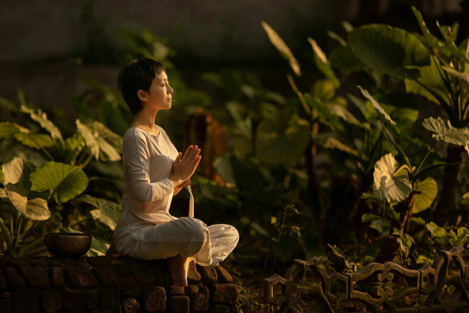 Serene scene of a woman meditating in a lush garden setting at daylight.
