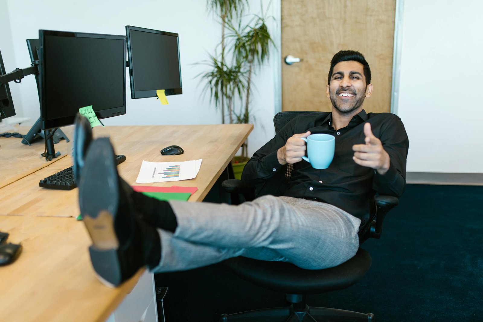 Smiling man relaxes in office with a mug, showing a casual work environment.